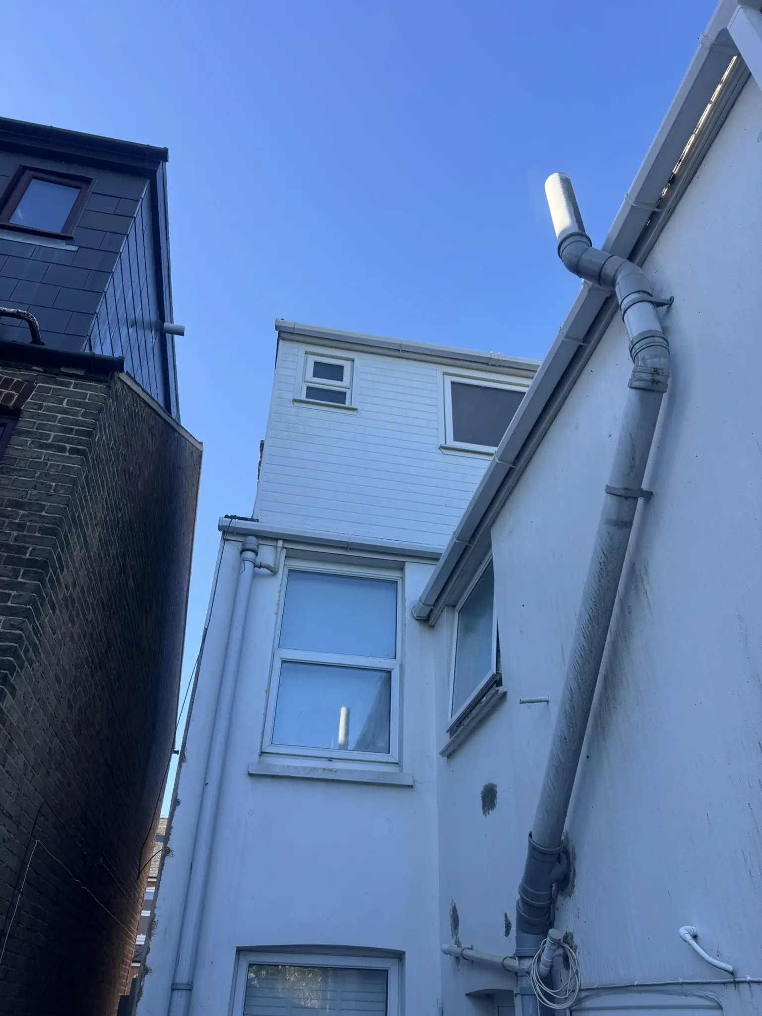 Cleaned white fascias, soffits and cladding with grey downpipes on a three-storey rendered property in Kent